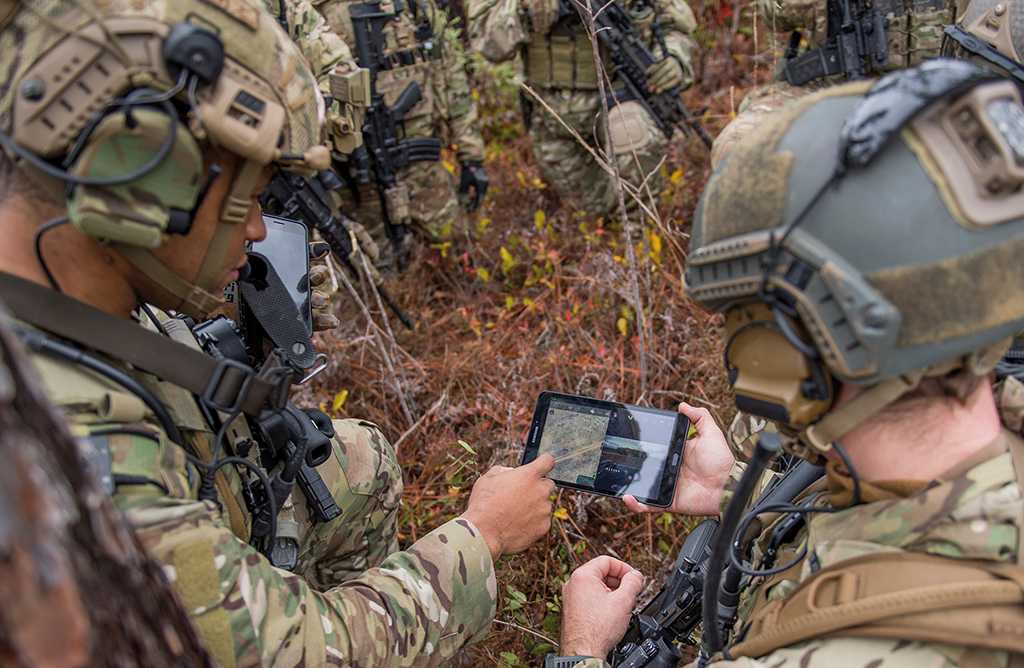 Mehrere Soldaten gucken auf ein Tablet, das einer von ihnen in der Hand hält.